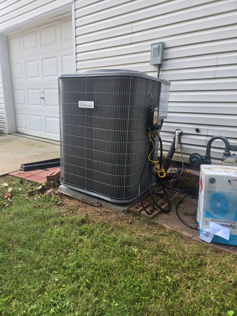 Digital manifold gauges connected to an outdoor condenser with an R-454B refrigerant carton beside the pad